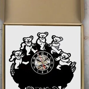 May include: A black vinyl record clock featuring five dancing bears with a clock face in the center. The clock face has black numbers and hands. The bears are surrounded by roses.