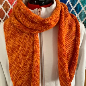 May include: A knitted scarf in a bright orange and red color gradient. The scarf is displayed on a white mannequin with a zipper.
