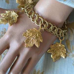 Peut inclure: Un bracelet à breloques en or avec un design de chaîne à maillons et plusieurs breloques en forme de feuilles.