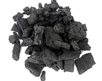 May include: A pile of dark charcoal pieces, varying in size and shape, against a white background. The charcoal appears to be made of wood, with visible grain and texture. The pieces are a deep black color.