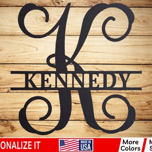 May include: Black metal monogram with the letter K and the name KENNEDY in a split design. The monogram is on a wood background.