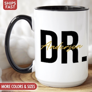 May include: White ceramic coffee mug with a black rim and handle. The mug has black text that says "DR. Anderson" in a bold font.