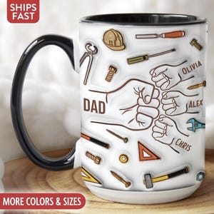 May include: White ceramic mug with a black handle and rim, featuring a design with tools, fists, and the word "DAD." Names "Olivia," "Alex," and "Chris" are also included. The mug has a glossy finish.