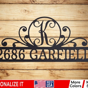 May include: Black metal house number and name sign with a decorative scroll design and a circle with the letter K in the center. The sign reads "2686 GAREFIELD".