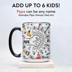 K&ouml;nnte beinhalten: Wei&szlig;e Keramiktasse mit schwarzem Henkel und Rand. Die Tasse zeigt das Wort "PAPA" und Illustrationen von Werkzeugen und F&auml;usten. Der Text "ADD UP TO 6 KIDS!" steht oben, mit Namen wie Alex und Olivia.
