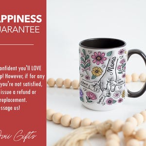 Op de afbeelding: Witte keramische mok met een zwart handvat en rand, versierd met kleurrijke bloemen en het woord "Mama". De mok heeft een hand-vasthoudend ontwerp met de namen "Chris", "Sophia" en "Ava". De tekst "Happiness Guarantee" is ook zichtbaar.