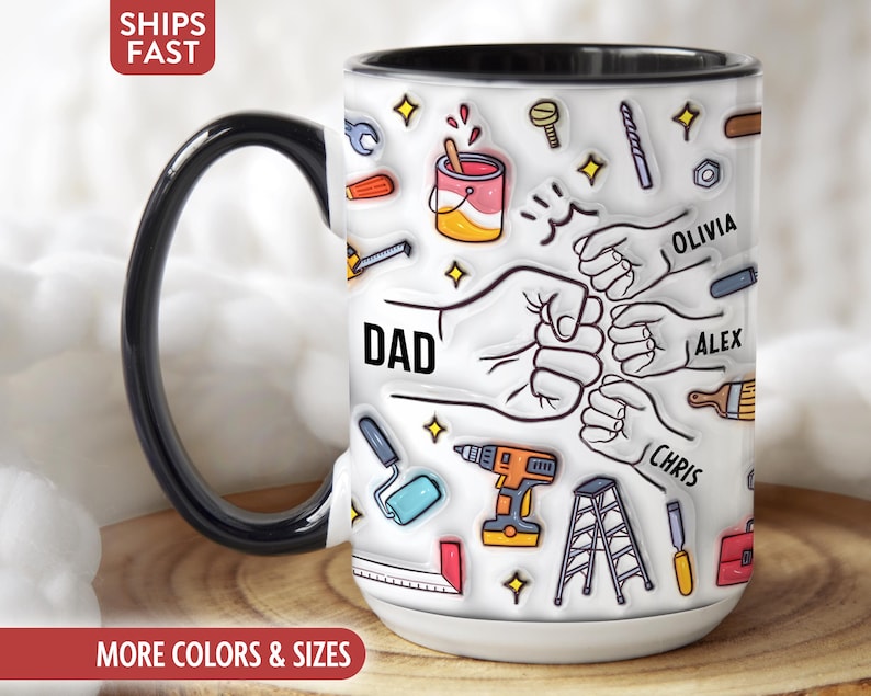 May include: White ceramic mug with a black handle and rim, featuring a design of tools, fists, and the word "DAD." Names "Olivia," "Alex," and "Chris" are also printed on the mug. The mug has a white base and a black handle.