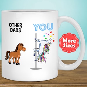 May include: White ceramic coffee mug with a humorous design. The left side of the mug says "Other Dads" and depicts a brown horse. The right side of the mug says "You" and depicts a unicorn on a pole with rainbow colours. The text "More Sizes" is in a red circle on the mug.