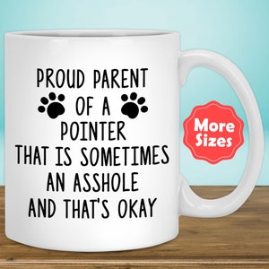 May include: White ceramic coffee mug with black text that reads "Proud Parent of a Pointer That is Sometimes an Asshole and That's Okay". Two black paw prints are above the word "Pointer". A red circle with white text that reads "More Sizes" is in the upper right corner of the image.