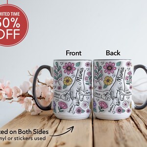 Op de afbeelding: Witte keramische mok met een zwarte handgreep en rand, met een bloemenontwerp met het woord "Mama" en namen. De mok is aan beide zijden bedrukt en heeft een "50% OFF" promotie. De mok staat op een houten oppervlak.