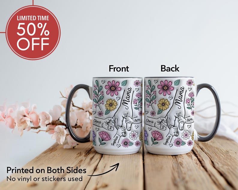 Op de afbeelding: Witte keramische mok met een zwarte handgreep en rand, met een bloemenontwerp met het woord "Mama" en namen. De mok is aan beide zijden bedrukt en heeft een "50% OFF" promotie. De mok staat op een houten oppervlak.