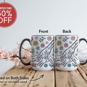 May include: White ceramic mug with a black handle. The mug has a floral design with a hand-drawn illustration of hands holding each other. The text "Grandma" is written on the mug. The mug is printed on both sides.