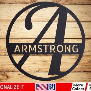 May include: A black metal circle with the letter "A" in a cursive font and the word "ARMSTRONG" across the center. The circle is on a wood background.