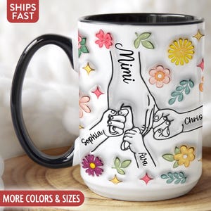 May include: White ceramic coffee mug with a black handle and black rim. The mug features a design of stylized hands with the names Mimi, Sophia, Ava, and Chris. The design is surrounded by colorful flowers and leaves.