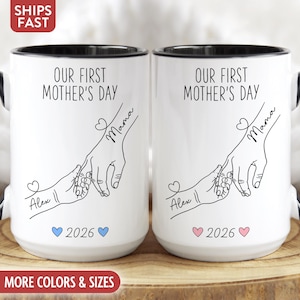 May include: Two white ceramic mugs with black rims and handles. Each mug features the text "OUR FIRST MOTHER'S DAY" and a line drawing of hands holding each other. The mugs also have the name "Mama" and "Alex" with a heart and the year 2026.