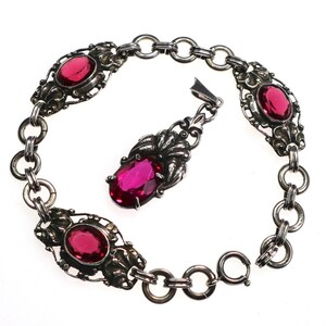 May include: A silver bracelet with a pendant featuring a red gemstone. The bracelet has a chain link design and four red gemstones set in ornate silver settings.