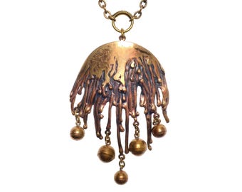May include: A unique, handcrafted pendant necklace. The pendant features a bronze-colored, abstract design with a textured, dripped appearance. Small, round, bronze-colored beads hang from delicate chains. The necklace has a bronze chain and clasp.