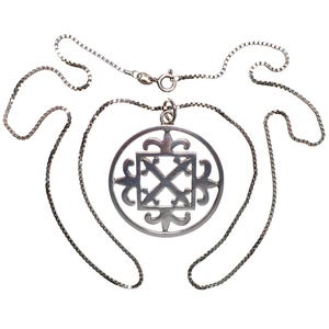 May include: A silver chain necklace with a pendant featuring a circular design with a stylized cross inside. The pendant has a detailed, intricate pattern.