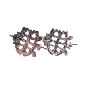 May include: A pair of copper-toned metal earrings featuring an intricate, openwork design with a circular frame and intersecting linear patterns. The earrings have a dark, oxidized finish and are attached to thin metal ear wires for hanging.