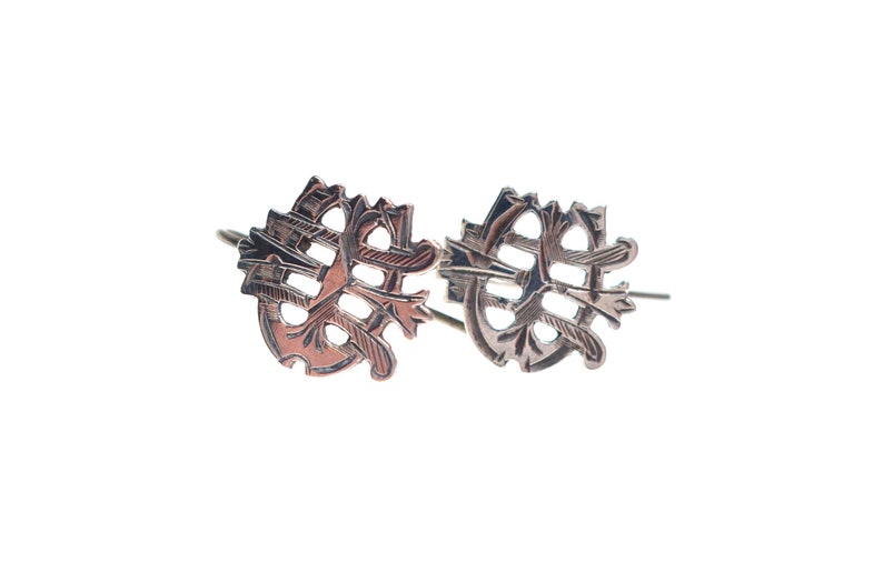 May include: A pair of copper-toned metal earrings featuring an intricate, openwork design with a circular frame and intersecting linear patterns. The earrings have a dark, oxidized finish and are attached to thin metal ear wires for hanging.