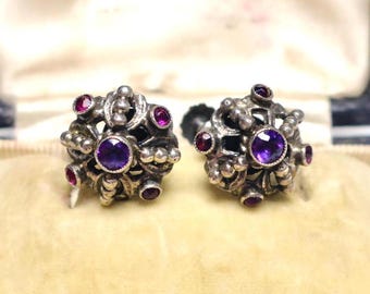 May include: A pair of silver earrings with intricate designs and purple and pink gemstones.