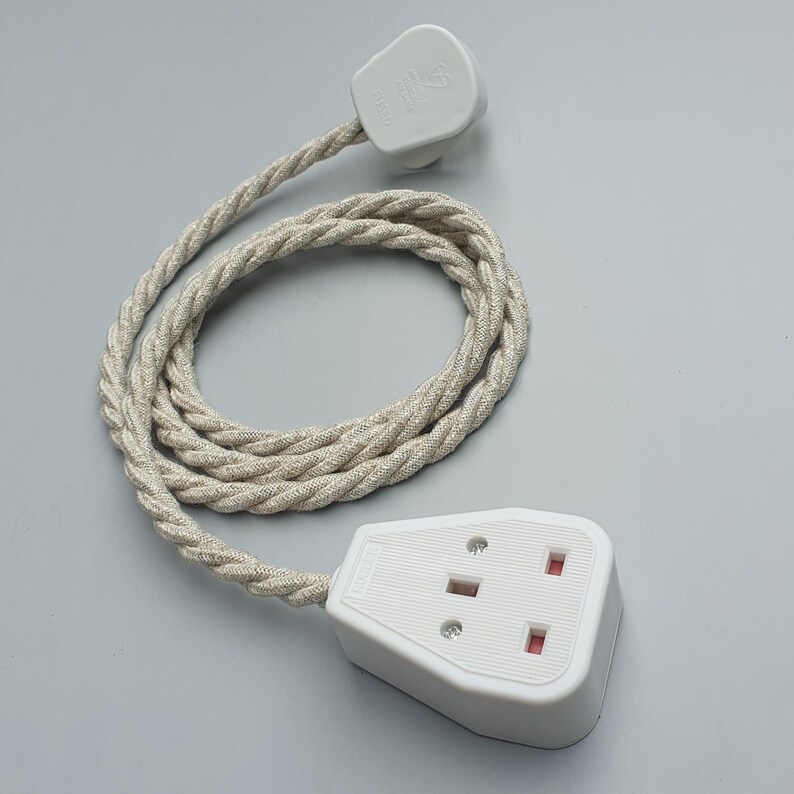 Op de afbeelding: Een witte stekker en stopcontact met een beige gevlochten snoer. Het stopcontact heeft drie gaten en rode accenten. Het snoer is opgerold en de stekker zit bovenaan. De achtergrond is effen lichtgrijs.