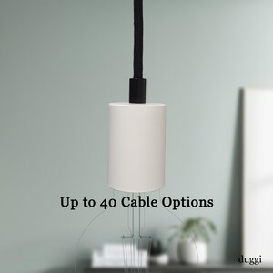 May include: A white cylindrical pendant light fitting with a black cord and a black top. The text "Up to 40 Cable Options" is displayed below the fitting. The fitting is suspended against a light green background.