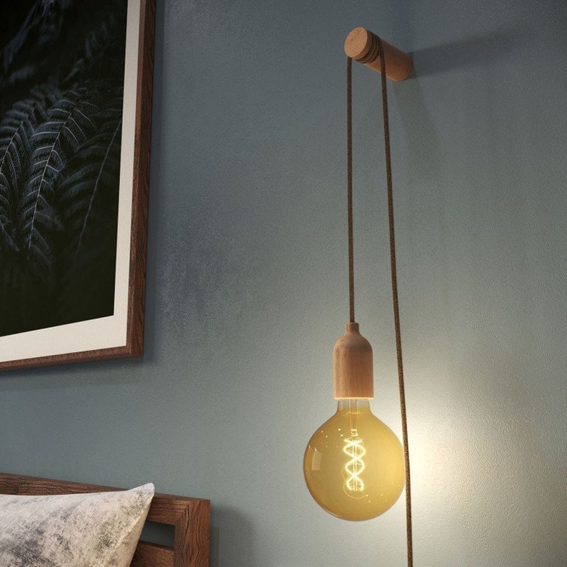 May include: A wooden wall-mounted light fixture with a brown cord and a clear glass bulb with a warm white glow.