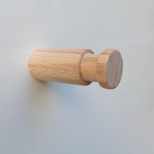 May include: A wooden wall hook with a round knob. The hook is light brown and made of natural wood.