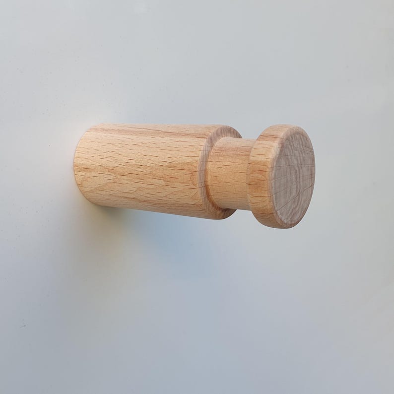 May include: A wooden wall hook with a round knob. The hook is light brown and made of natural wood.