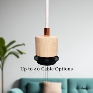 May include: A modern pendant light fitting featuring a cylindrical wooden body, a copper-toned detail, and a white fabric cable. The text "Up to 40 Cable Options" is visible. The light hangs from the ceiling.