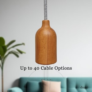 May include: A wooden pendant light with a bottle-shaped design, suspended by a grey fabric-covered cord. The text "Up to 40 Cable Options" is displayed below the light. The light fixture is a modern design.