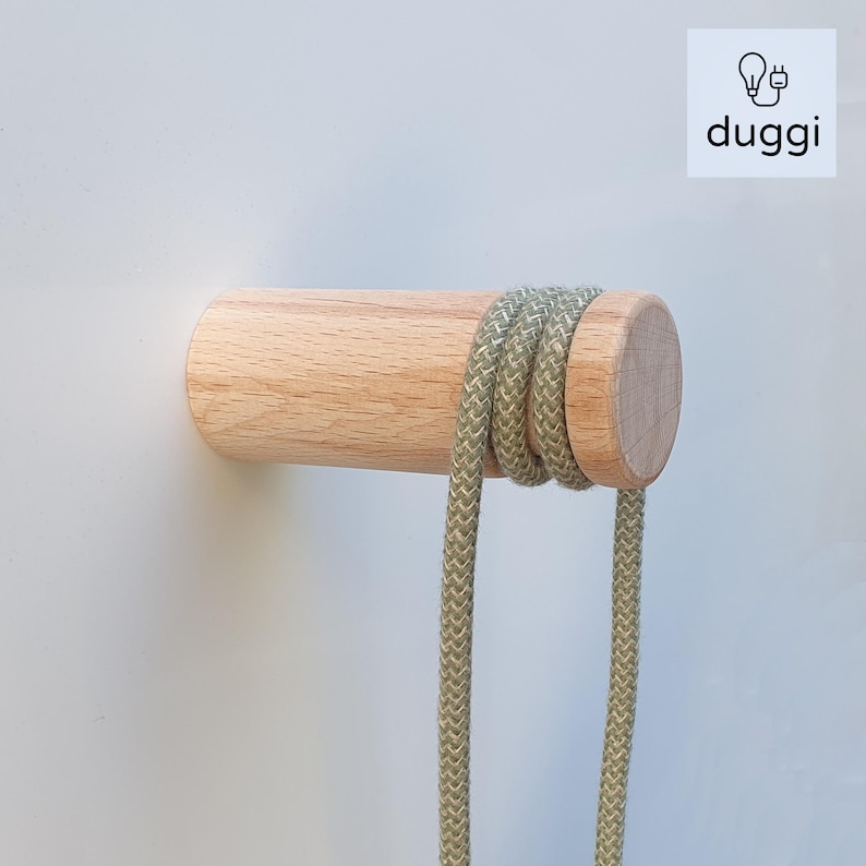 May include: A wooden wall hook with a light green cord wrapped around it. The hook is mounted on a white wall.