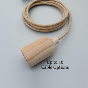 May include: A light-coloured wooden pendant light fitting with a matching beige fabric-covered cord. The text "Up to 40 Cable Options" is printed on the image. The fitting is cylindrical with a rounded top.