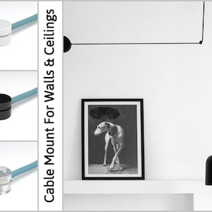 May include: Image shows cable mounts in white, black, and clear, with a light blue cable. The text reads "Cable Mount For Walls & Ceilings" and "DUGGI DESIGN". A black and white framed picture of a dog is on a white shelf.