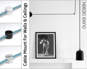 May include: Image features cable mounts in white, black, and clear, with a light blue cable. The text reads "Cable Mount For Walls & Ceilings" and "DUGGI DESIGN". A black and white framed picture of a dog is on a white shelf.
