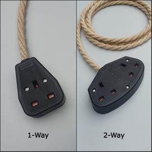 Op de afbeelding: Twee zwarte stopcontacten met rode inzetstukken en een beige gevlochten snoer. E&eacute;n stopcontact is gemarkeerd met "1-Way" en de andere met "2-Way". De stopcontacten zijn van rubber en hebben zilveren schroeven. Het snoer is opgerold.