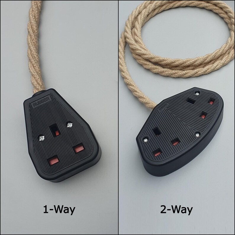 Op de afbeelding: Twee zwarte stopcontacten met rode inzetstukken en een beige gevlochten snoer. E&eacute;n stopcontact is gemarkeerd met "1-Way" en de andere met "2-Way". De stopcontacten zijn van rubber en hebben zilveren schroeven. Het snoer is opgerold.