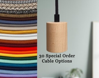 Op de afbeelding: Een cilindrische houten pendelarmatuur met een zwarte kabel. De afbeelding toont ook een verscheidenheid aan kleurrijke, met stof bedekte elektrische kabels. Tekst op de afbeelding luidt "30 Special Order Cable Options."