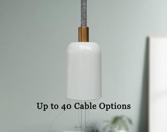 May include: A white pendant light fixture with a gold-colored base and a gray fabric-covered cord. The text "Up to 40 Cable Options" is displayed below the light fixture. The light fixture is hanging in front of a blurred background.
