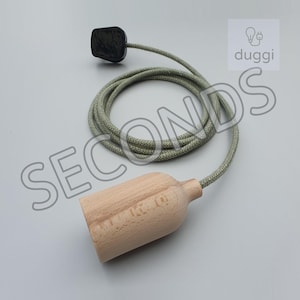May include: A wooden pendant light fitting with a green fabric cable and a black plug. The fixture has the word "SECONDS" in large grey letters and the brand name "duggi".