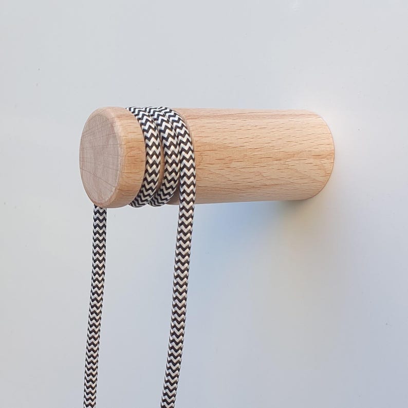 May include: A wooden wall hook with a black and white chevron patterned cord wrapped around it. The hook is mounted on a white wall.