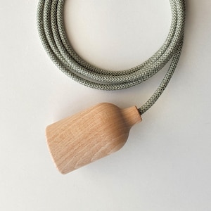 May include: A wooden light fitting with a natural finish is attached to a grey braided cord. The cord is coiled, and the fitting is cylindrical with a wider base. The light fixture is designed for use in a home or office setting.