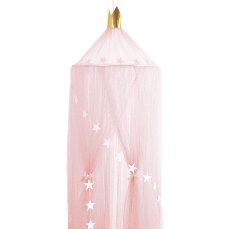 Pode incluir: Um dossel de tule rosa com uma coroa dourada no topo e estrelas brancas penduradas no tule.