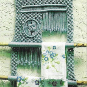 Op de afbeelding: Een macramé wandhanger met een blauw en wit bloemenpatroon. Twee handdoeken met een bloemenpatroon hangen onder de macramé. De handdoeken hebben de tekst "Towel Haven, Pattern on Page 24".