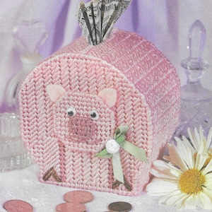 May include: Pink crocheted piggy bank with a green ribbon and a white button. The piggy bank is filled with cash and coins.
