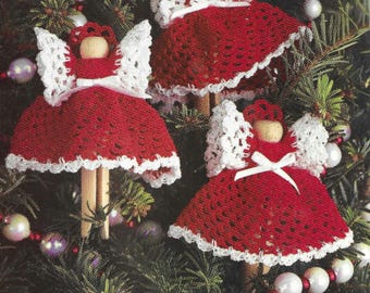 May include: Three crocheted angel ornaments with white wings and red dresses. The angels are hanging on a Christmas tree.