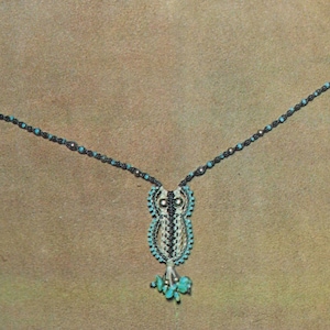 Könnte beinhalten: Eine türkisfarbene und schwarze Perlenkette mit einem Eulenanhänger. Die Eule besteht aus weißen und schwarzen Perlen und hat türkisfarbene Akzente.