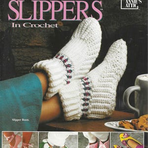 May include: A crochet pattern book titled "Simple Slippers in Crochet" with a photo of white crocheted slippers on a model's feet. The book cover also features a photo of four different styles of crocheted slippers: ballerina, elf, star stitch, and pansy.