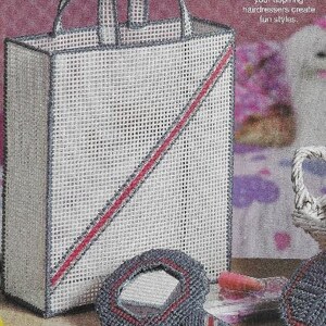 Pode incluir: Uma bolsa tote de lona branca com um design de listras vermelhas e cinzas. A bolsa tem uma alça e está sentada em uma mesa com um espelho de mão cinza e vermelho e outras ferramentas de penteado.